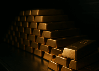 Lingotes de oro apilados en una bóveda oscura con luz suave resaltando el brillo frontal